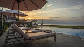 Zona de piscina con sillones, sombrillas y vista al mar al atardecer.