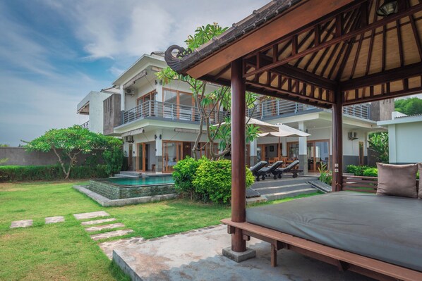 A two-story house with a covered outdoor seating area, a swimming pool, and lush greenery.