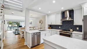 A modern kitchen with white cabinetry, a stainless steel range hood, and a large island.