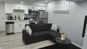 Eine moderne Küche mit weißen Schränken, Edelstahlgeräten und einem schwarzen Sofa mit gemusterten Kissen.
