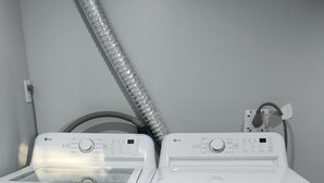 Zwei weiße LG Waschmaschinen mit Frontlader in einem Waschraum mit grauer Wand und grauem Boden.