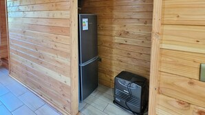 Interior de una cabaña de madera con un refrigerador empotrado y un calentador portátil.