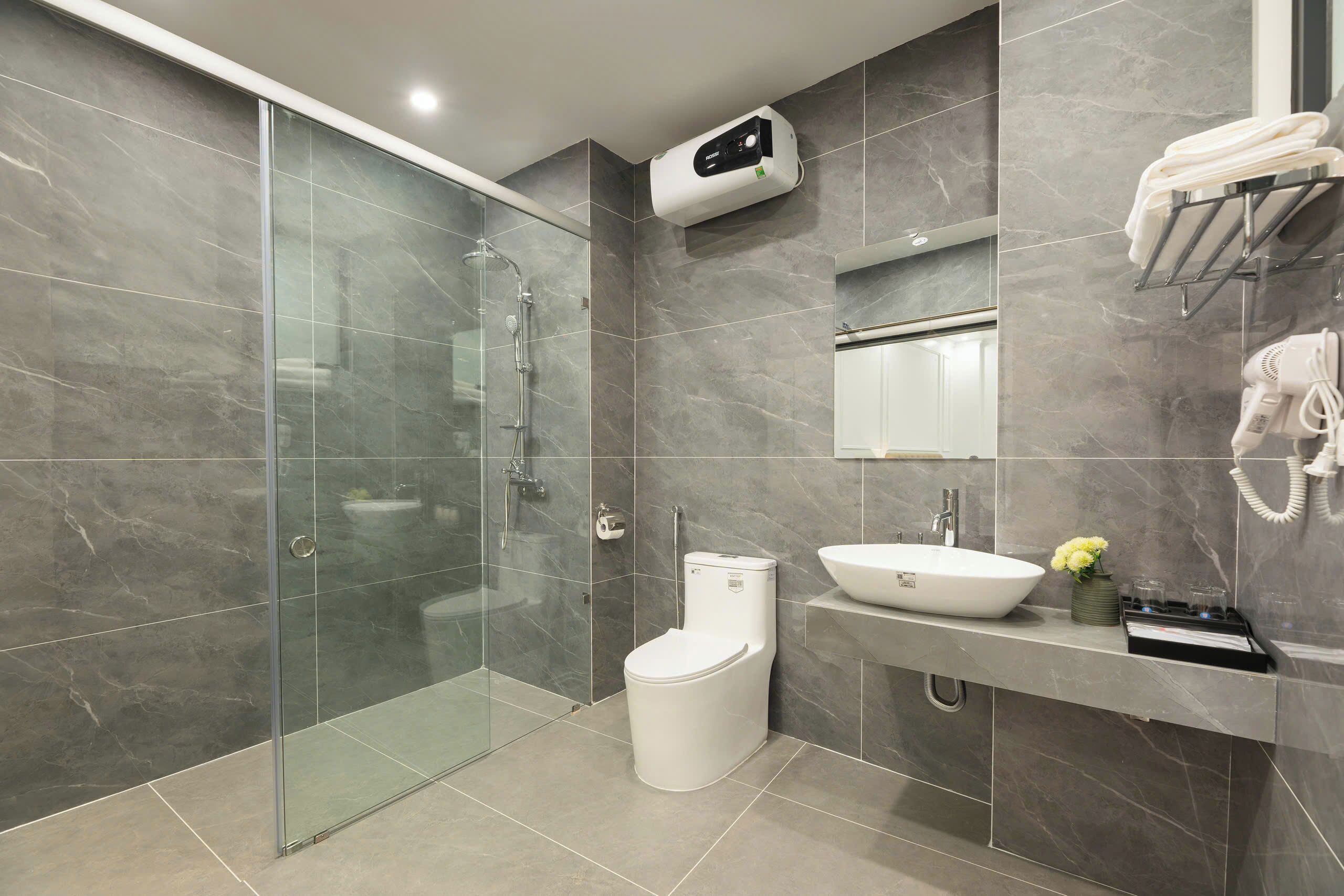A modern bathroom with a glass shower enclosure, a white toilet, a vanity with a sink and a mirror, and a towel rack.