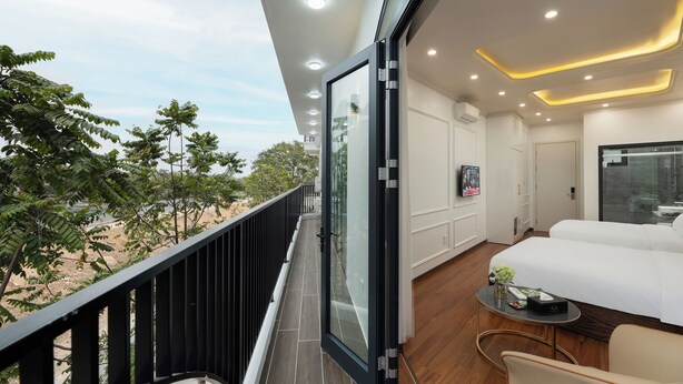 Habitación de hotel moderna con balcón, cama, una mesita y vistas a palmeras.