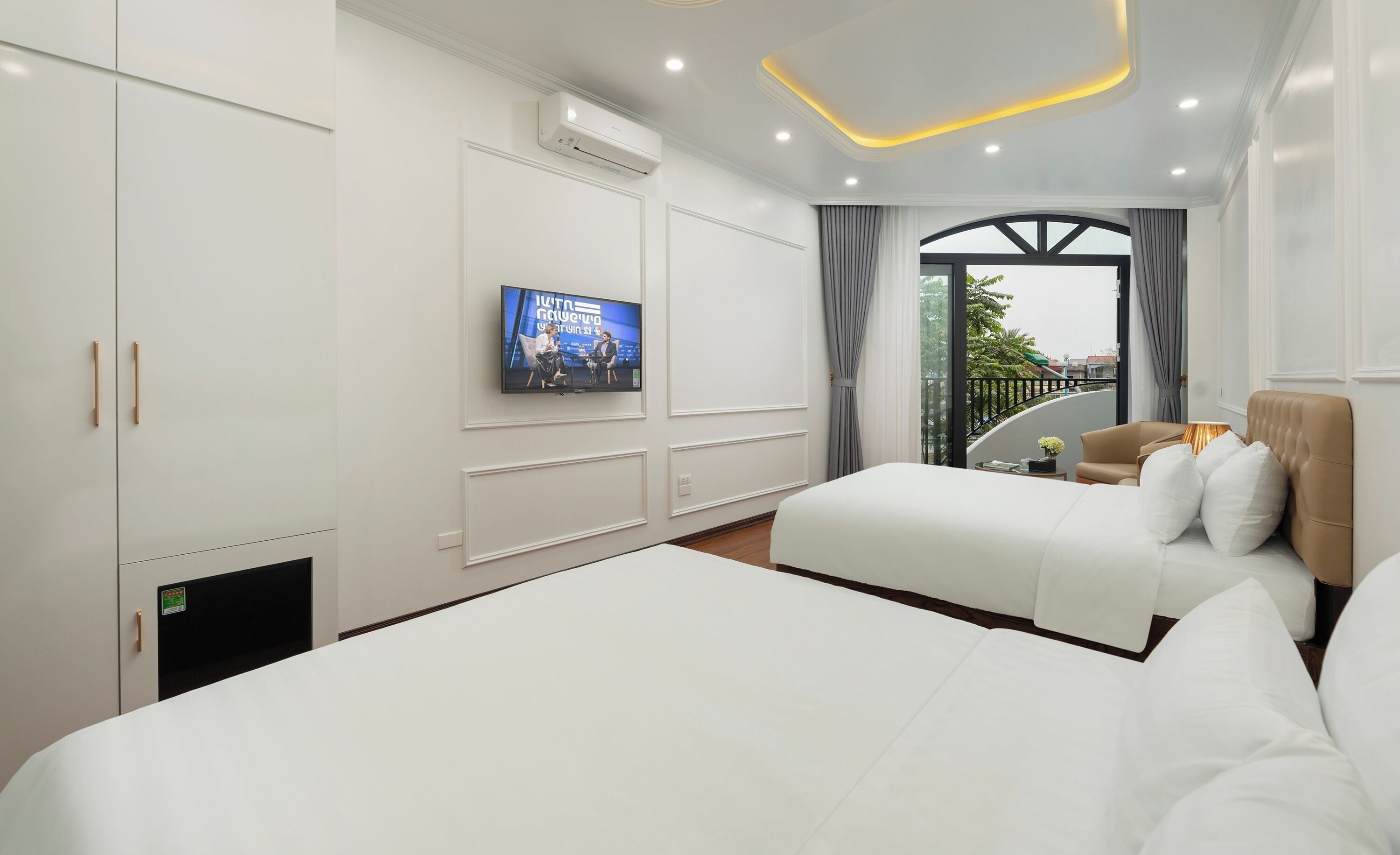 A hotel room with two beds, a TV on the wall, and a balcony with a view.