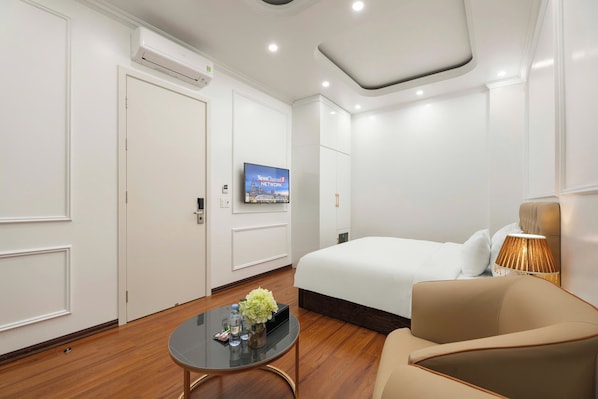 Habitación de hotel con cama, televisor, mesita de café y una florera con botella de agua, y una lámpara.