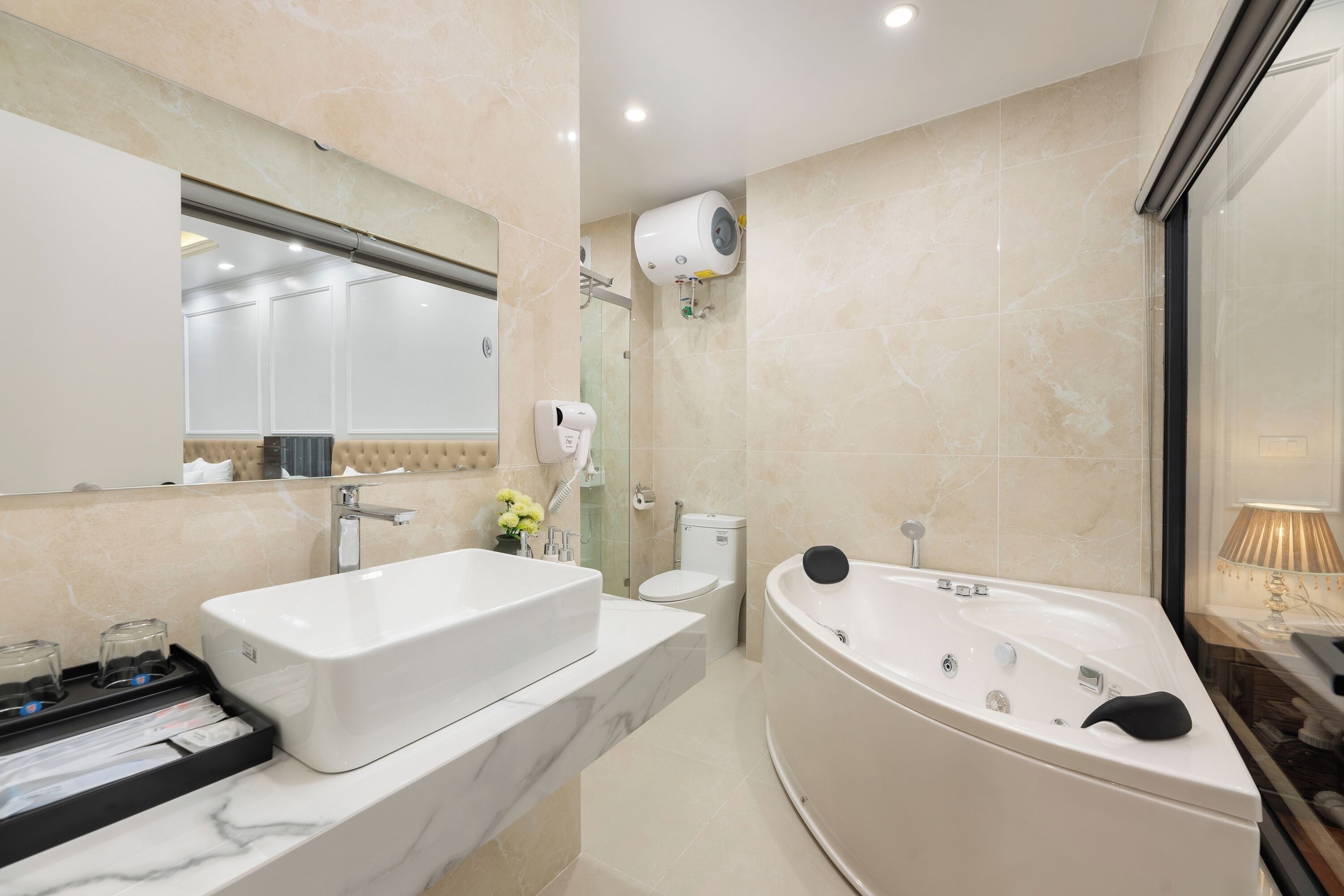 A modern bathroom with a large bathtub, a sink, a toilet, and a hairdryer mounted on the wall.