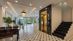 Vestíbulo de hotel con piso de baldosas geométricas, una araña, una escalera y un mostrador de recepción.