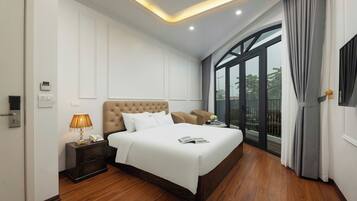 A modern hotel room with a large bed, a bedside table with a lamp, a nightstand, and a view of the outdoors through a large window.
