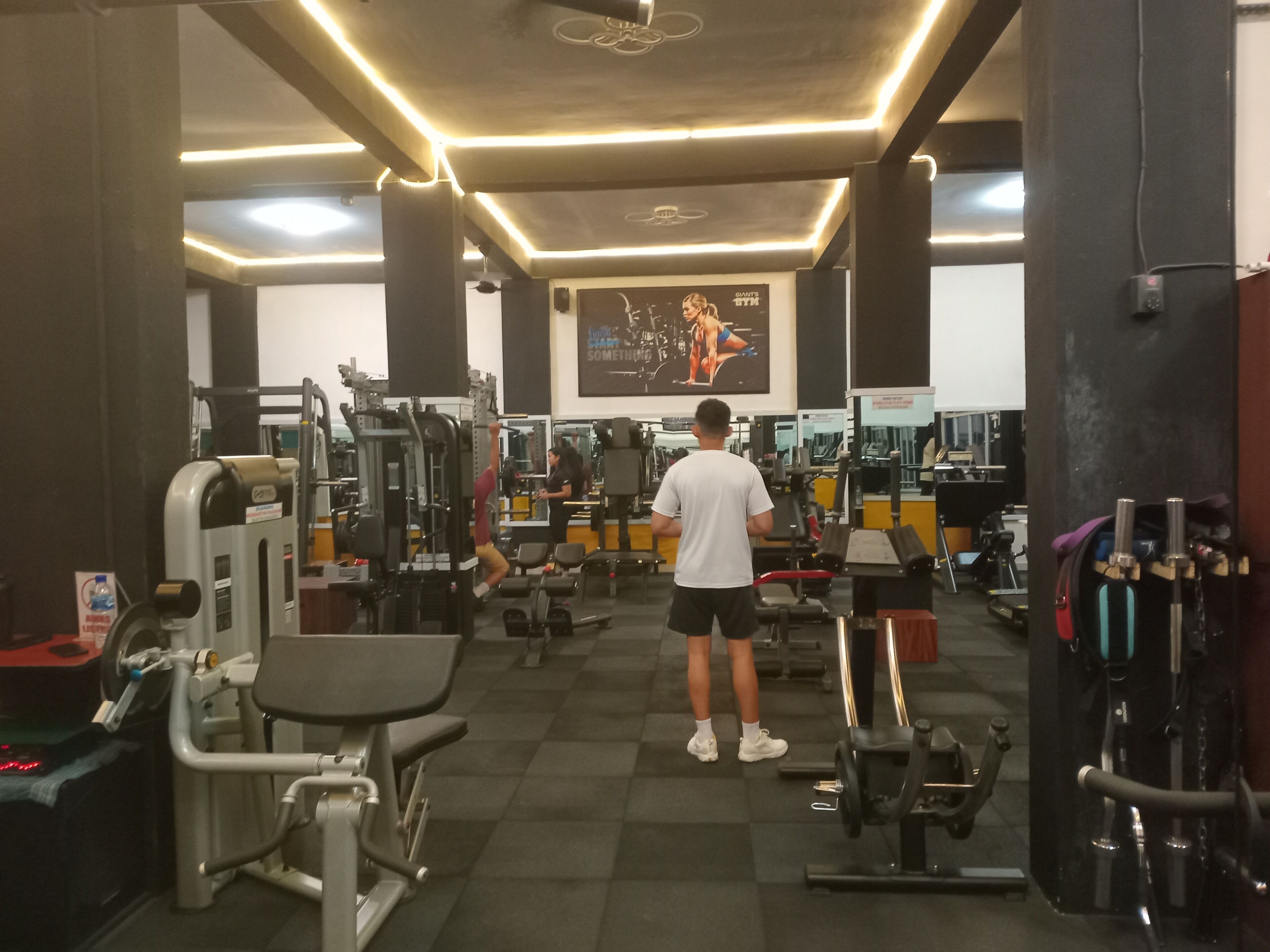 A gym with various exercise machines, a large mirror, and a motivational poster on the wall.