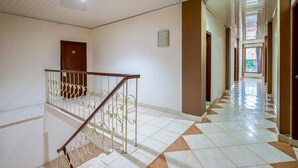 Un pasillo espacioso con suelo de baldosas, una puerta de madera y una escalera con barandillas de metal decorativo.