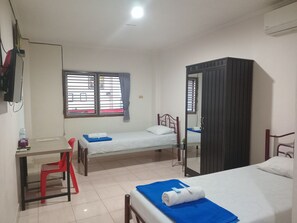 A room with two single beds, a desk with a chair, a wardrobe, and a window with blinds. - Hotel Bambu Kuning (Bandar Lampung)