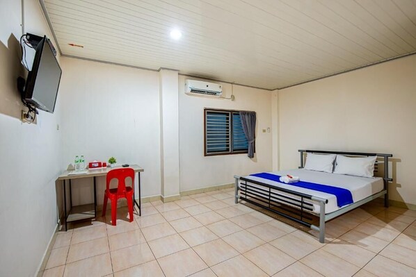 A bedroom with a bed, a desk with a chair, a TV, and an air conditioning unit.