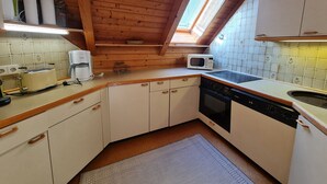 A compact kitchen with wooden ceiling beams, a skylight, white cabinets, a microwave, a toaster, and a coffee maker.