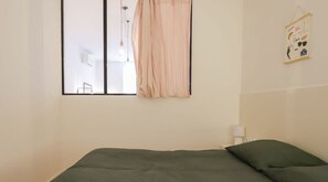 Un dormitorio con cama, ventana con cortinas, luz de pared y un pequeño adorno en la pared.