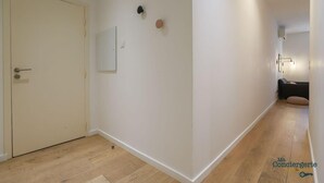 A hallway with a wooden floor, a closed door, and a wall-mounted light fixture.