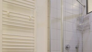 A shower with a glass door, a handheld showerhead, and a wall-mounted faucet.
