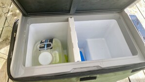 A caixa de refrigeração aberta contém uma garrafa de água, um recipiente azul e um recipiente branco.