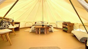Tenda com cama, mesa e cadeiras no interior.