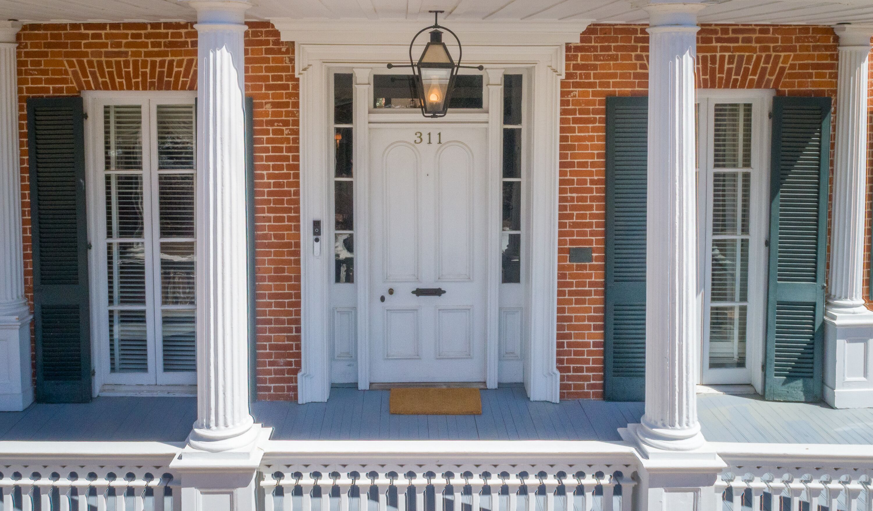 A white door with the number 311, flanked by two columns and green shutters, leading to a porch with a white railing.
