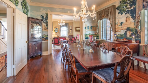 Comedor con una larga mesa de madera, sillas, un candelabro y un espejo grande.