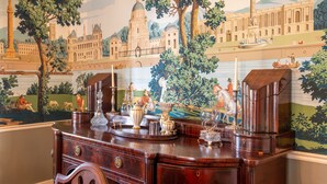 Un aparador de madera con cajones y un espejo, ubicado frente a una pared con un mural que representa una escena histórica.