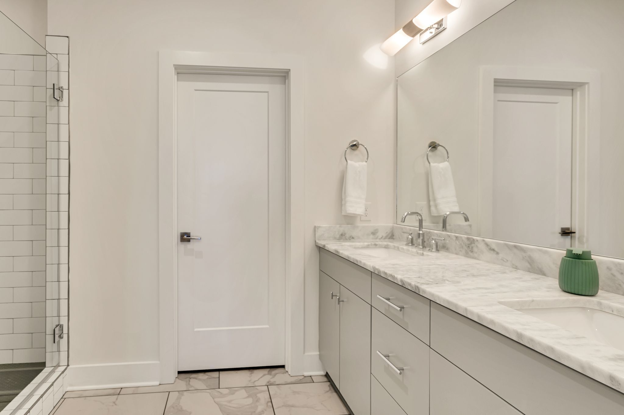 Een moderne badkamer met een witte deur, een wastafel met een marmeren aanrechtblad en een groene zeepdispenser.