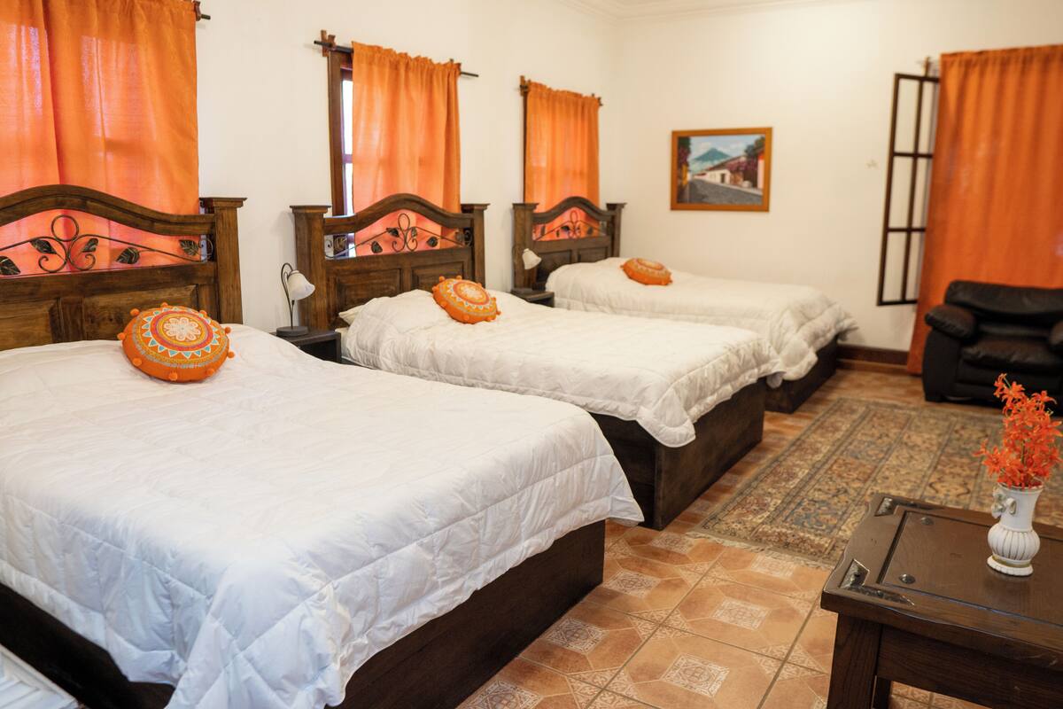 A hotel room with two beds, a wooden headboard, a small table with a vase, and a patterned rug.