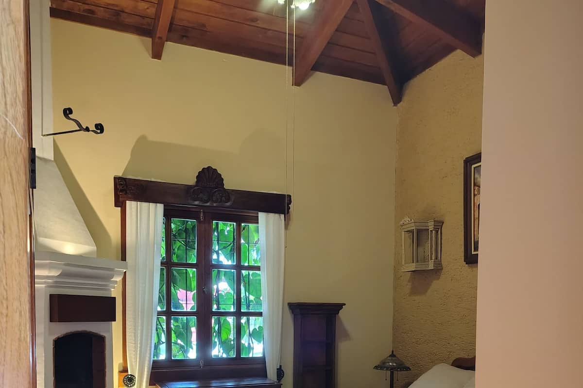 A bedroom with a bed, a window with curtains, a fireplace, and a ceiling fan.