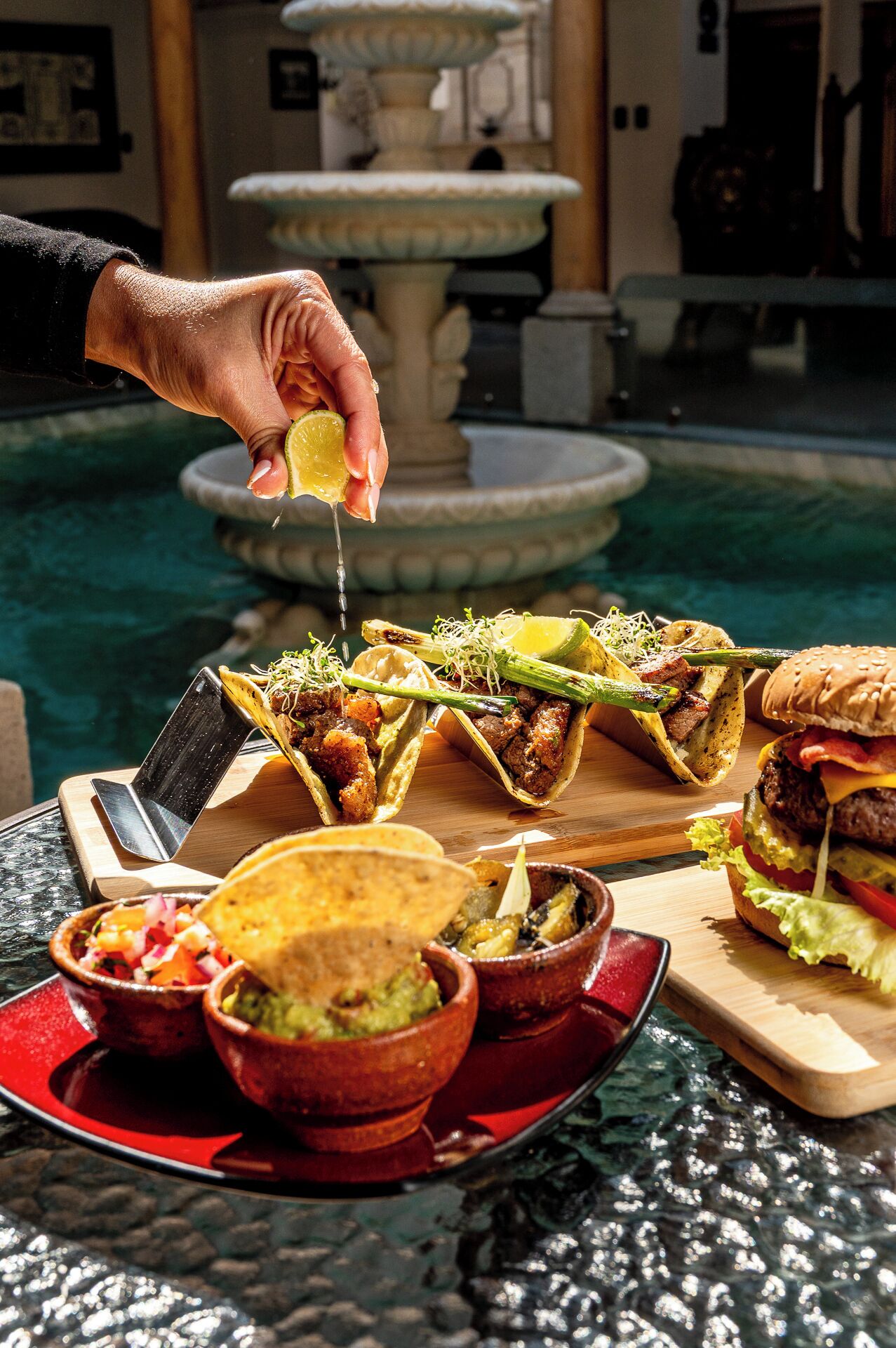 Una mesa de comedor con tacos, una hamburguesa y tazones de salsa y guacamole.