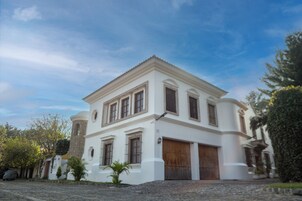 Un edificio de estilo colonial blanco con una torre central, grandes puertas de madera y un camino de adoquines.