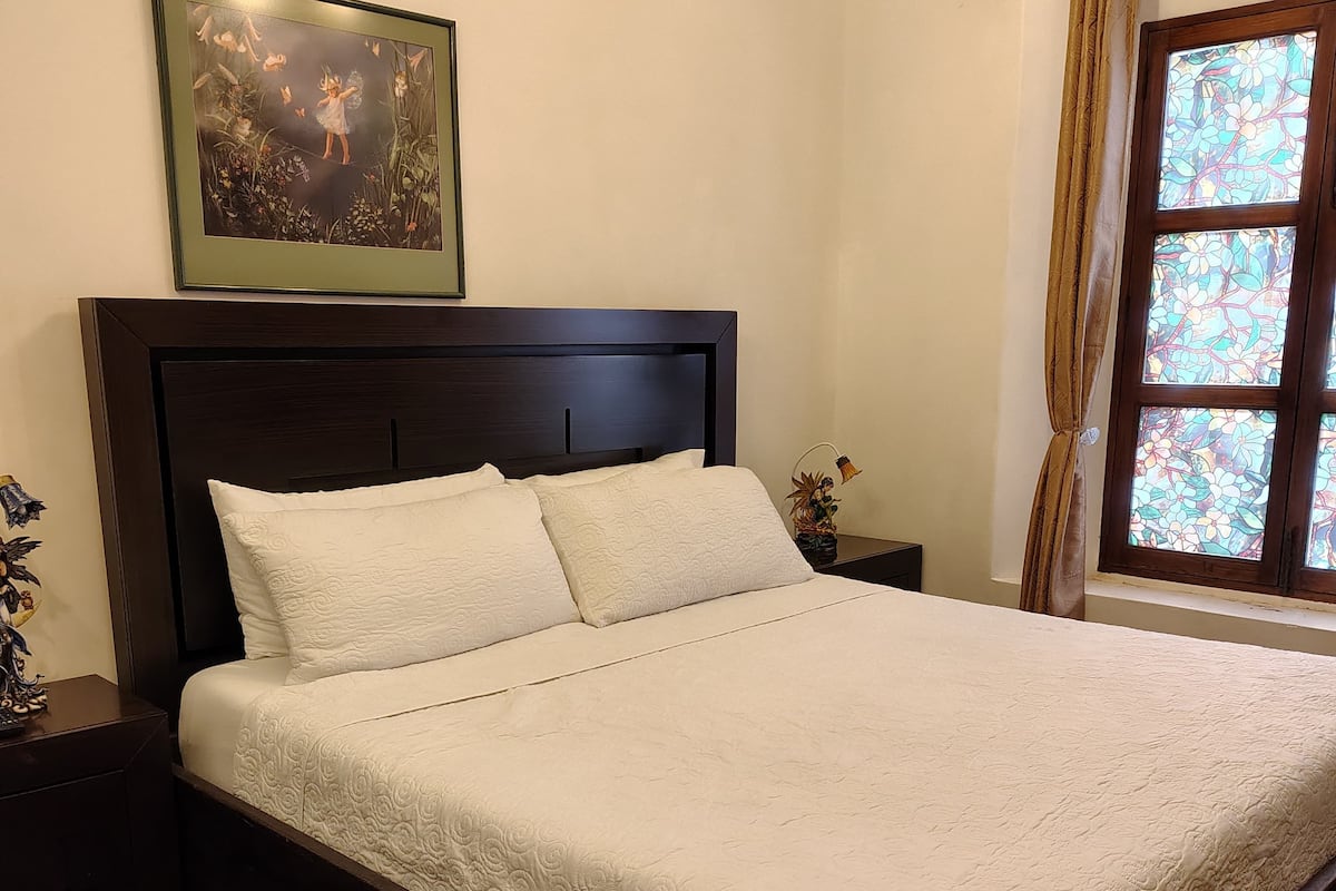 A bed with a dark headboard, white bedding, and a framed picture above it.