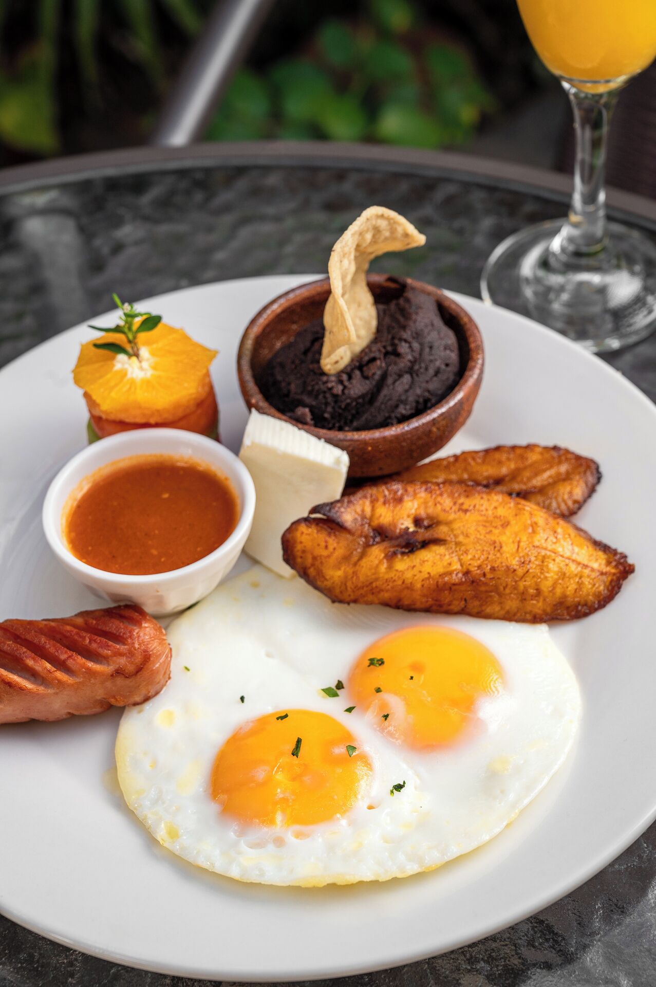 Een bord met ontbijt, waaronder eieren, plantains en een klein schaaltje saus.