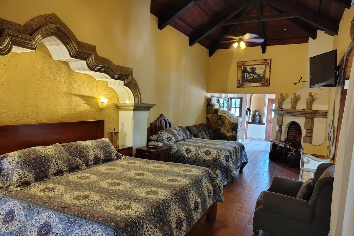 A hotel room with two beds, a wooden ceiling, a fireplace, and a television.