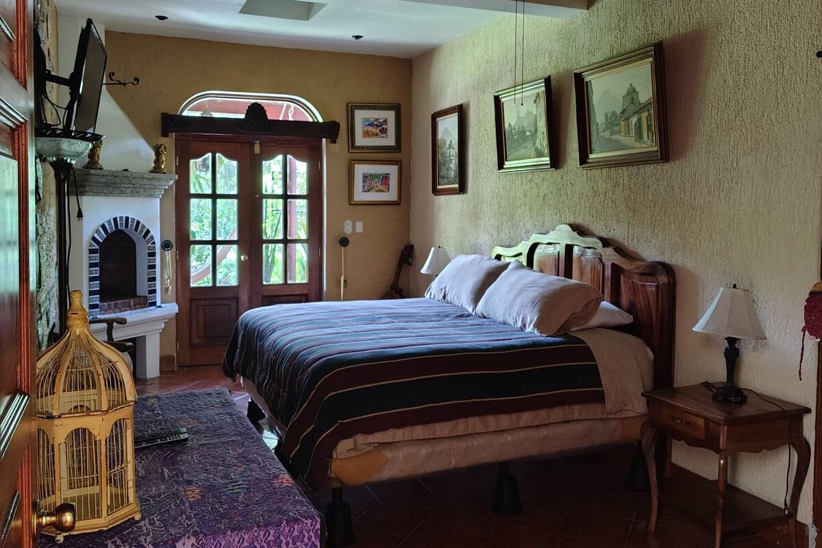 A bedroom with a large bed, a wooden headboard, a nightstand, a lamp, and a wall-mounted shelf.