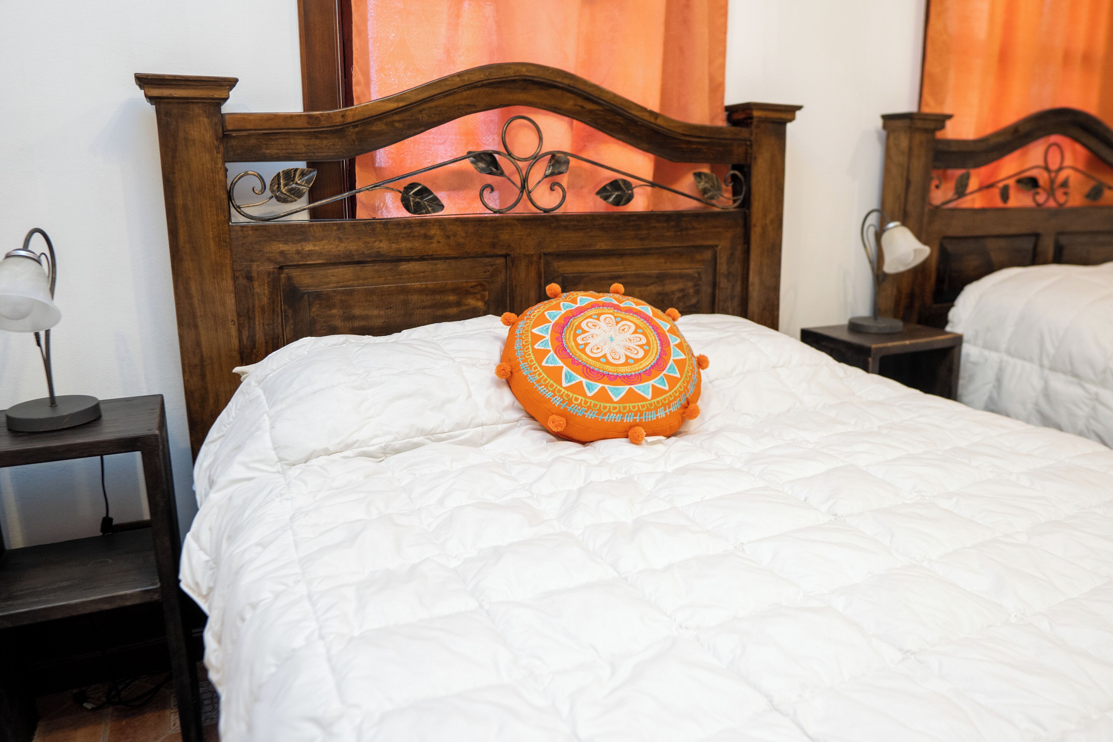 A neatly made bed with a decorative pillow, a bedside table with a lamp, and a wooden headboard.