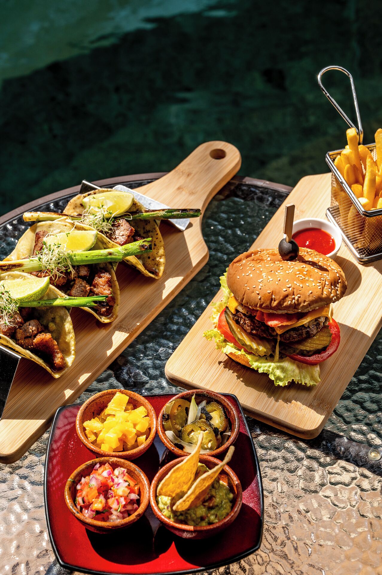 Eine Mahlzeit mit Tacos, einem Burger und verschiedenen Dips auf einem Tisch.