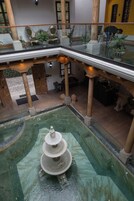 Un atrio de varios niveles con una fuente central, columnas de madera y plantas en macetas.