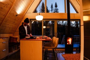A cozy cabin interior with a wooden ceiling, a dining area with a table and chairs, and a fireplace.