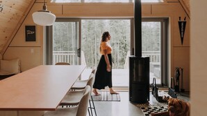 A room with a large table, a sofa, a standing heater, and a dog. - Canadian Classic | Spa • Sauna • Fire • Forest (Sainte-Lucie-des-Laurentides)