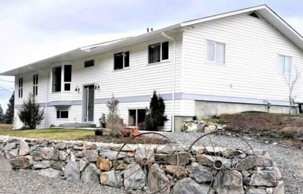 A two-story house with a stone wall in front, a garage, and a driveway. - Charming 2-bedroom suite in Lake Country with AC, WiFi.  (Lake Country)