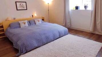 Une chambre à coucher avec un lit, une table de chevet, une lampe, une fenêtre avec des rideaux et un tableau encadré au mur.