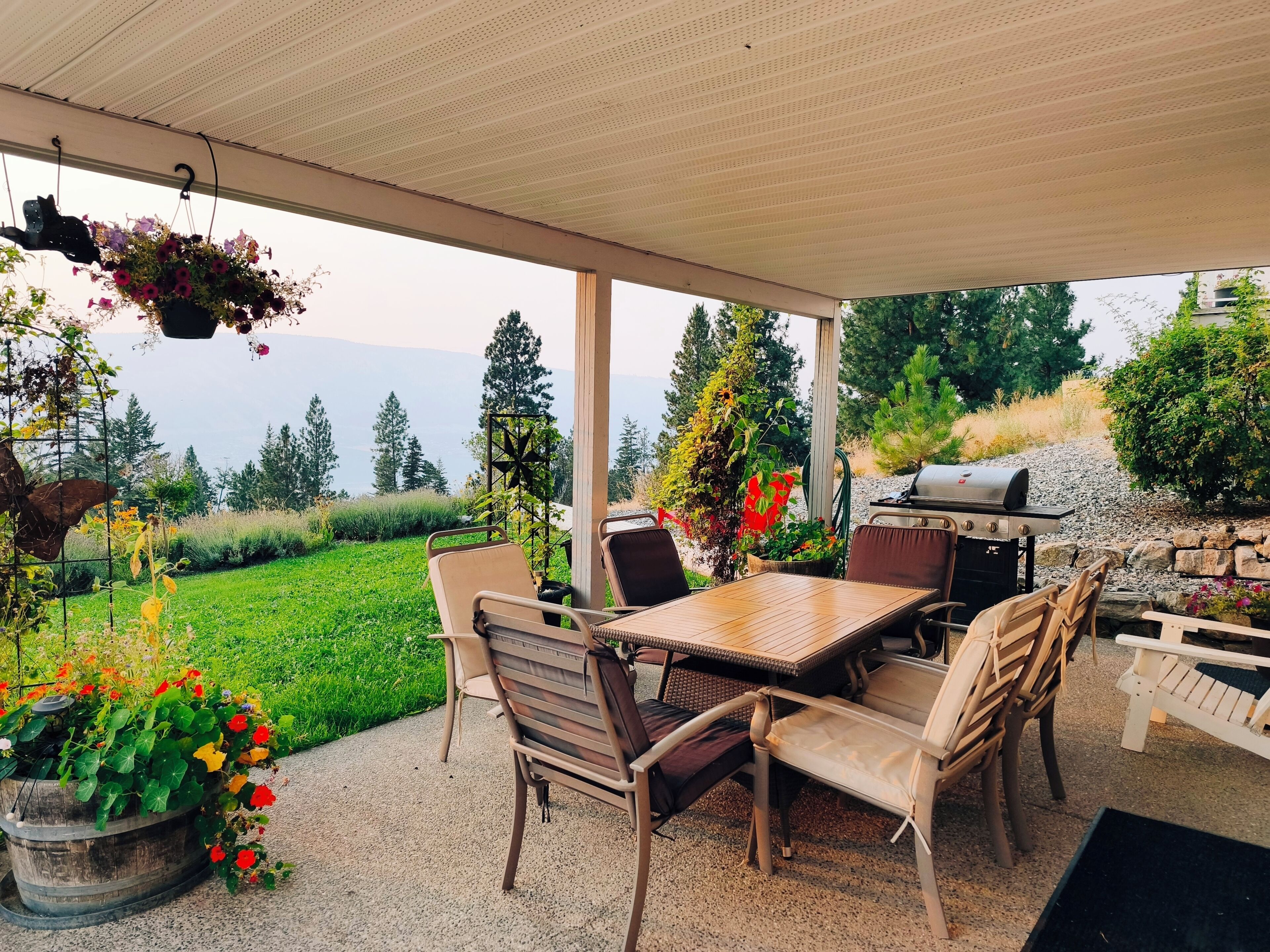 Un patio al aire libre con mesa y sillas, una parrilla y cestas de flores colgantes.