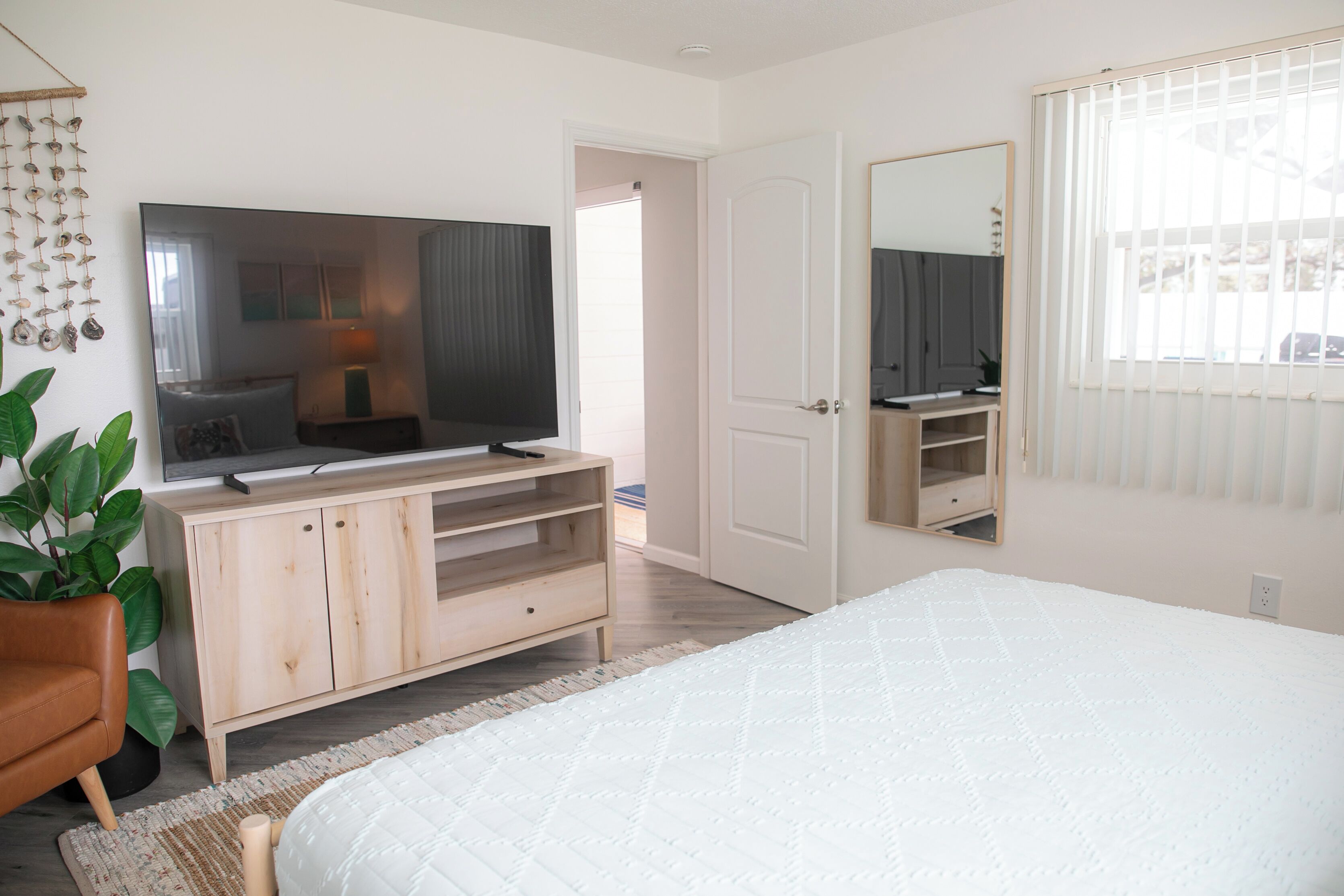 Ein Schlafzimmer mit Bett, Fernseher, Holzschrank, Spiegel und einer Zimmerpflanze.