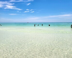 A beach with clear turquoise water and a few people swimming.