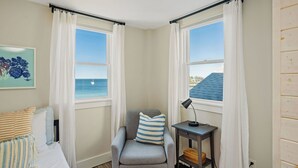 Ein Eckzimmer mit Meerblick, ein Sessel mit gestreiftem Kissen, ein Nachttisch mit Lampe und ein Bild an der Wand.