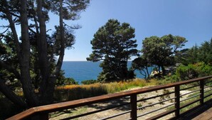 A coastal view with a wooden deck and railing, overlooking the ocean and dense trees.