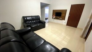 A living room with a black leather sofa, a flat-screen TV mounted on the wall, and a wooden door. - House with heated pool for up to 16 people close to the beach. (Três Marias)