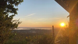A sunset view from a window overlooking a landscape with trees and a distant body of water. - House with heated pool for up to 16 people close to the beach. (Três Marias)