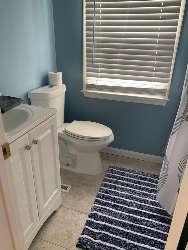 Une salle de bain avec des toilettes, un lavabo et une fenêtre avec des stores.